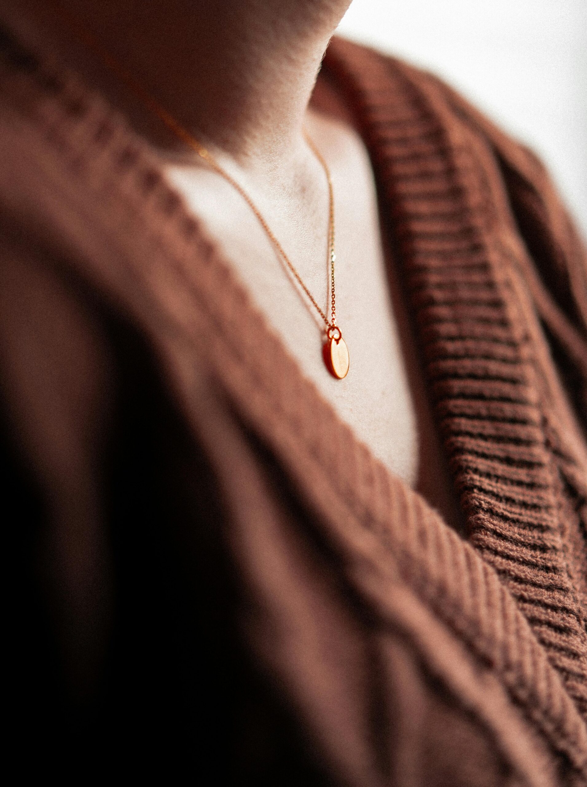 Close-up of a gold necklace with a pendant on a woman's neck wearing a brown sweater.